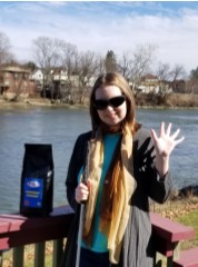 Erin waving Hi near a river and with a package of White Cane Coffee.